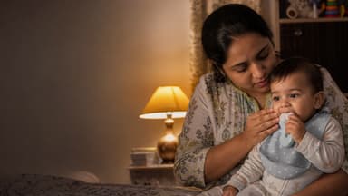 A mother holding a baby on her lap in lamplight while the baby chews a blue silicone teether