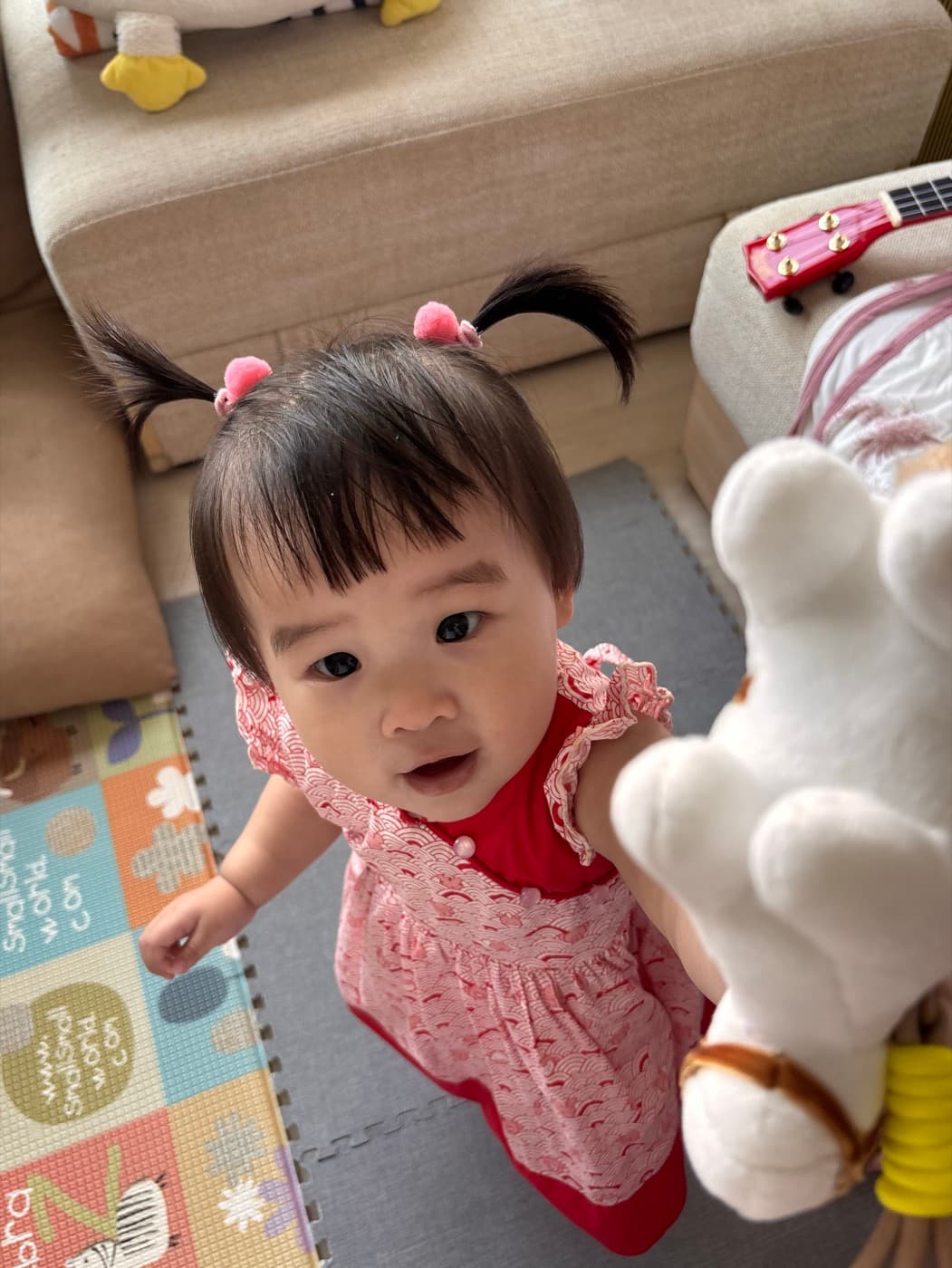 A baby sitting up on a playmat holding a soft rabbit toy