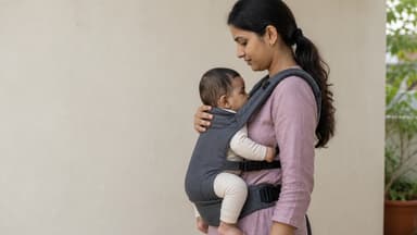 Side view of a mother carrying a baby high on her chest in a structured carrier, the baby's head clear of her chin