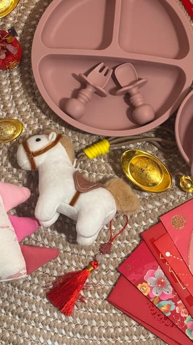 A Lunar New Year flatlay: red packets, gold ingots, mandarins, a horse toy and a Little Rei silicone plate