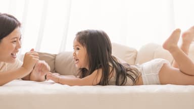 A mother and toddler playing on a bed, the toddler in Little Rei pull-up pants