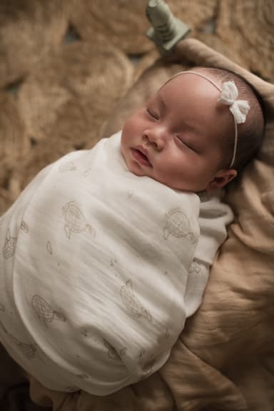 A newborn fast asleep, wrapped closely in a soft bamboo muslin