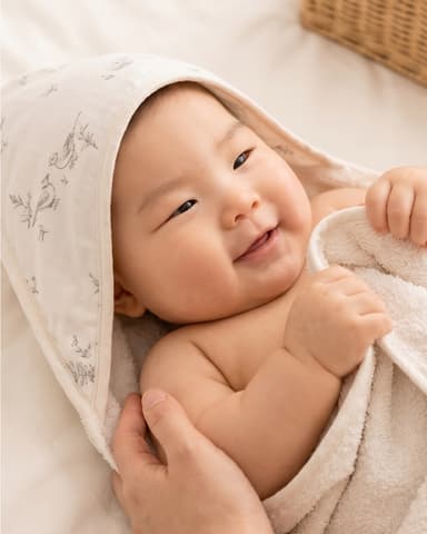A newborn wrapped in a Little Rei bamboo hooded towel, hands tucked under their chin