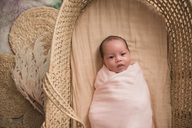 A newborn settled in a woven moses basket in a pale pink bamboo swaddle