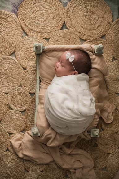 A swaddled newborn lying on jute rugs, wrapped firmly in a bamboo muslin