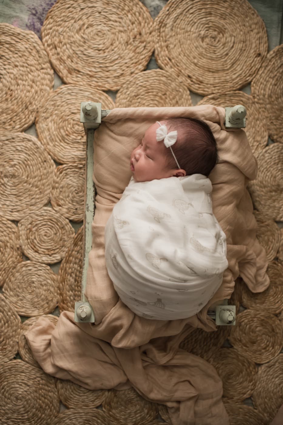 A swaddled newborn lying on jute rugs, wrapped firmly in a bamboo muslin