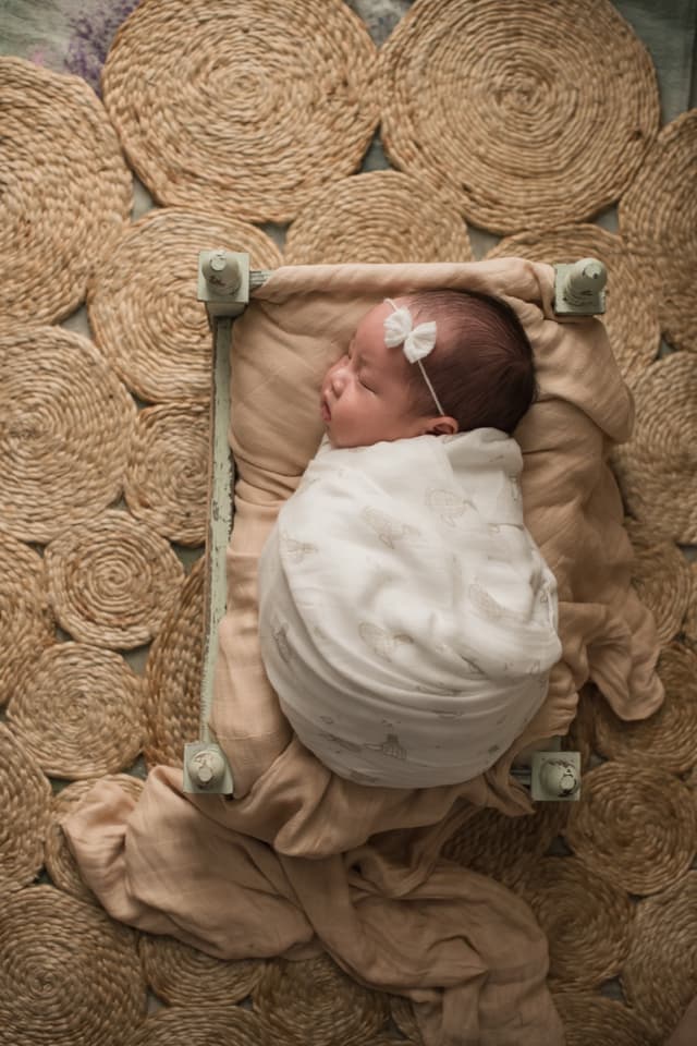 A swaddled newborn lying on jute rugs, wrapped firmly in a bamboo muslin