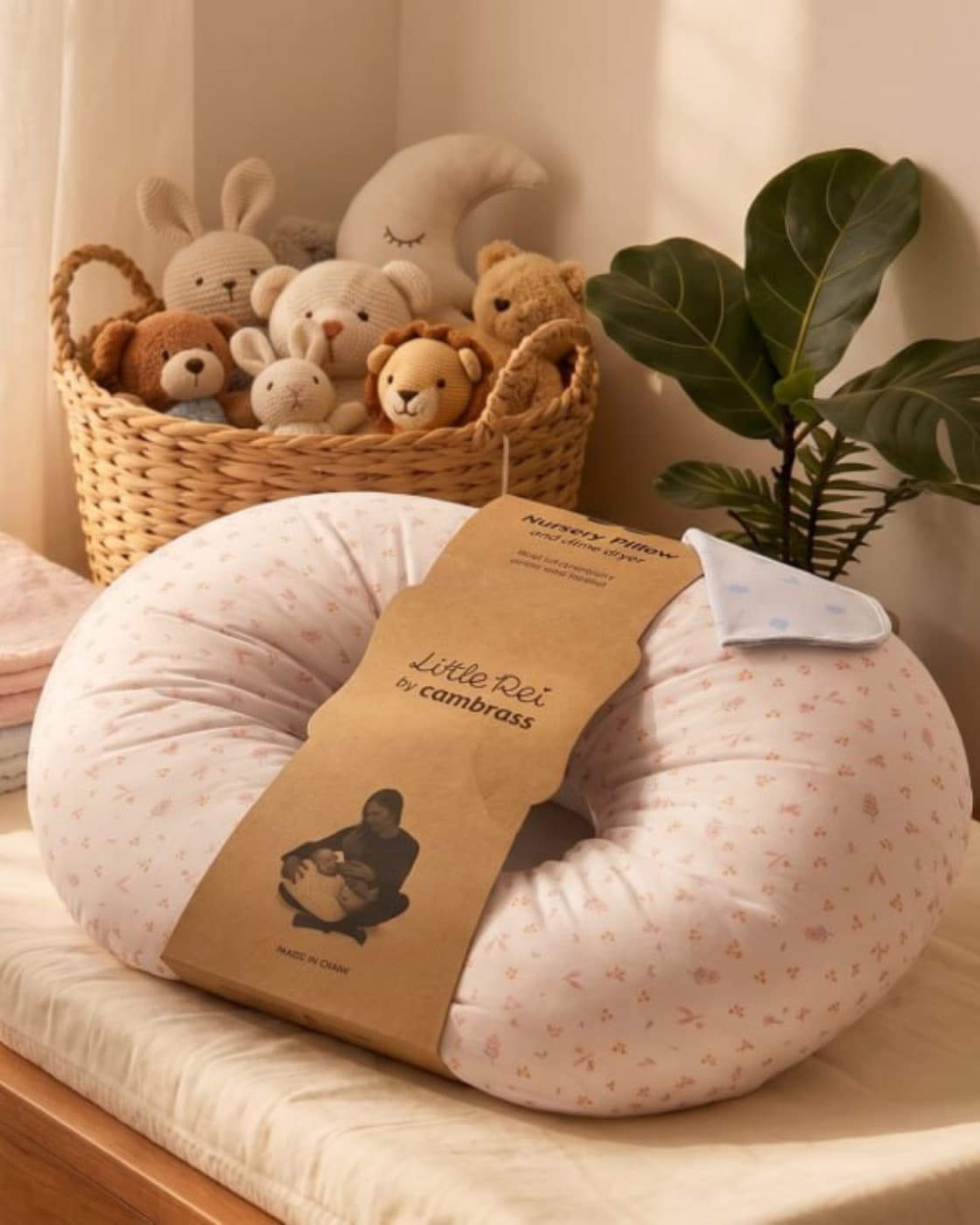 A nursery basket of soft toys beside a folded Little Rei nursing pillow
