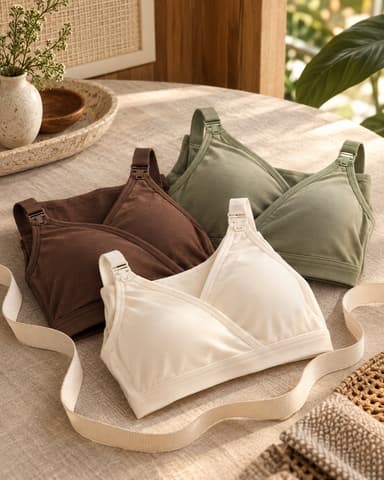 Three nursing bras in brown, sage and cream laid out on a linen tablecloth