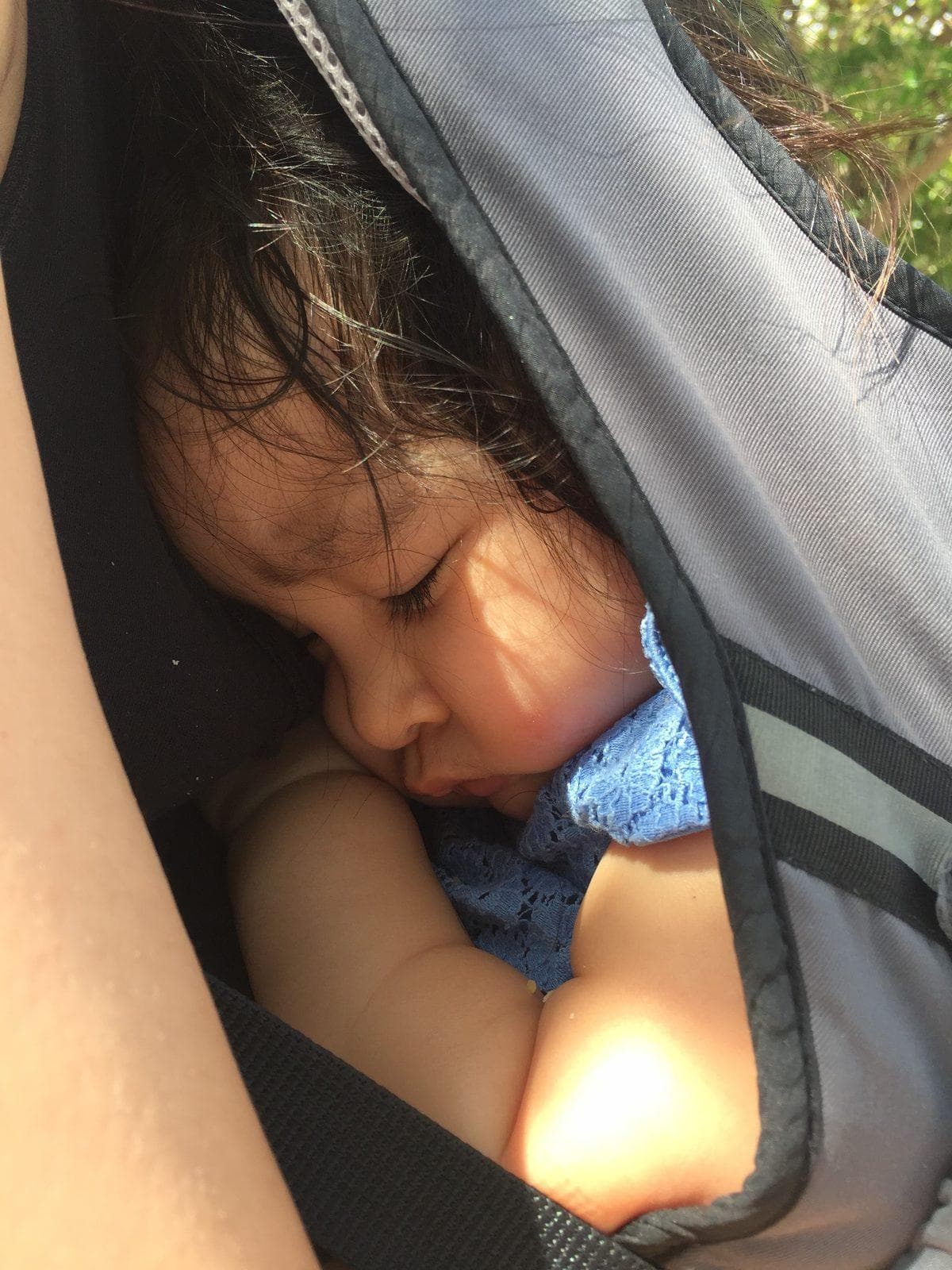Shan asleep against her mother's chest in a mesh-panelled carrier, face turned to the side