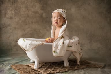 A small child sitting in a roll-top bath with a towel wrapped around their hair