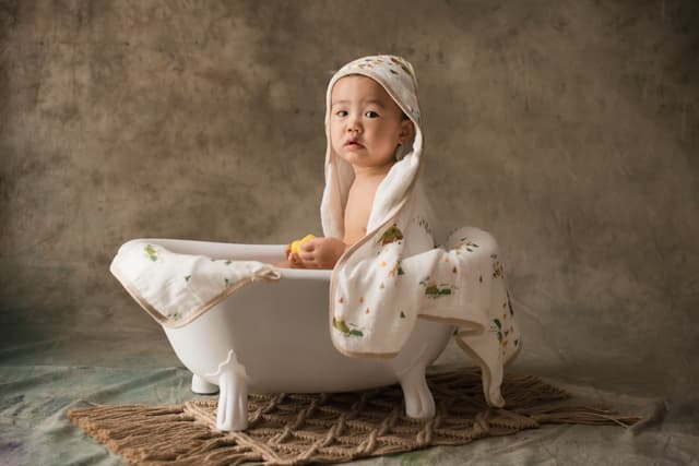 A small child sitting in a roll-top bath with a towel wrapped around their hair