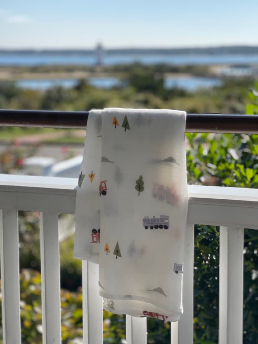 A Little Rei train-print bamboo muslin hanging on a balcony rail above open water