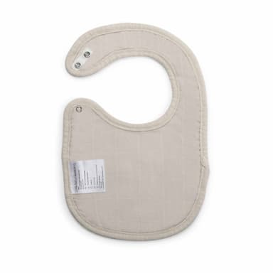 A sand-coloured bamboo muslin bib laid flat, showing its press-stud neck fastening