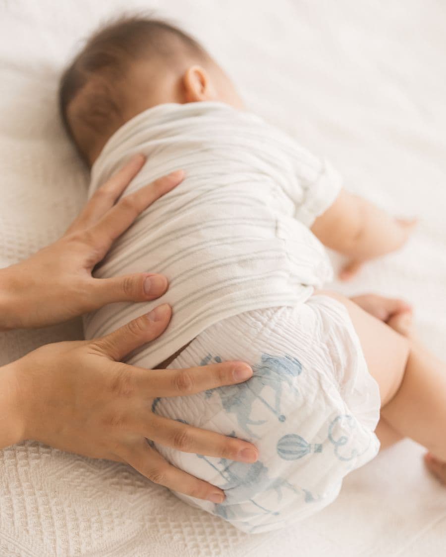 A parent's hands on their baby's back, the baby in a Little Rei diaper
