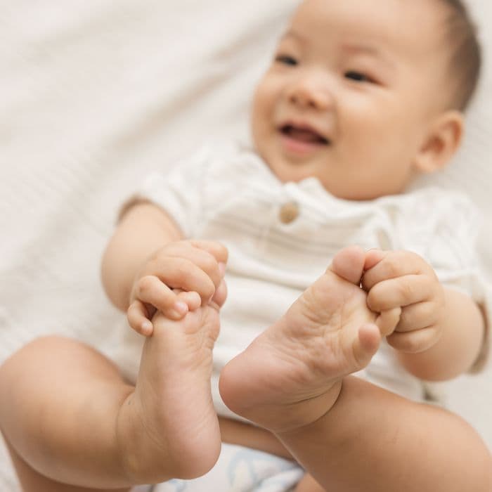 A smiling baby holding their feet, in a Little Rei tape diaper
