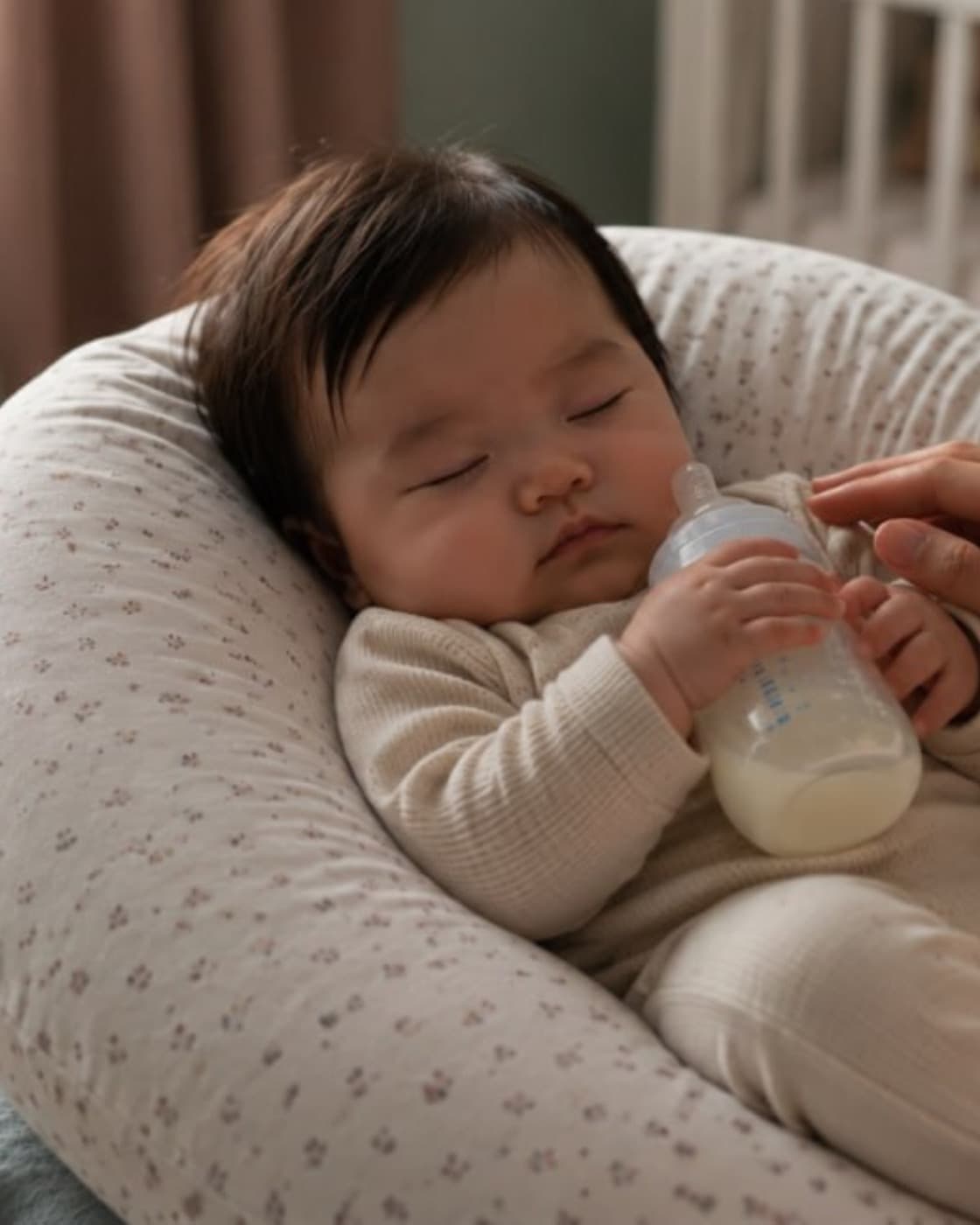 A baby dozing on a Little Rei nursing pillow while being offered a bottle