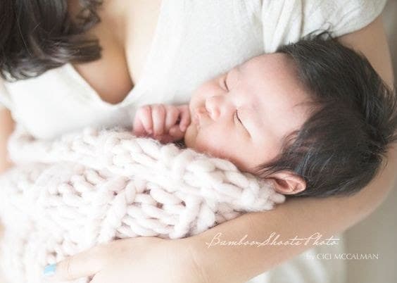 Newborn Shan asleep against her mother's chest, wrapped in a knit blanket