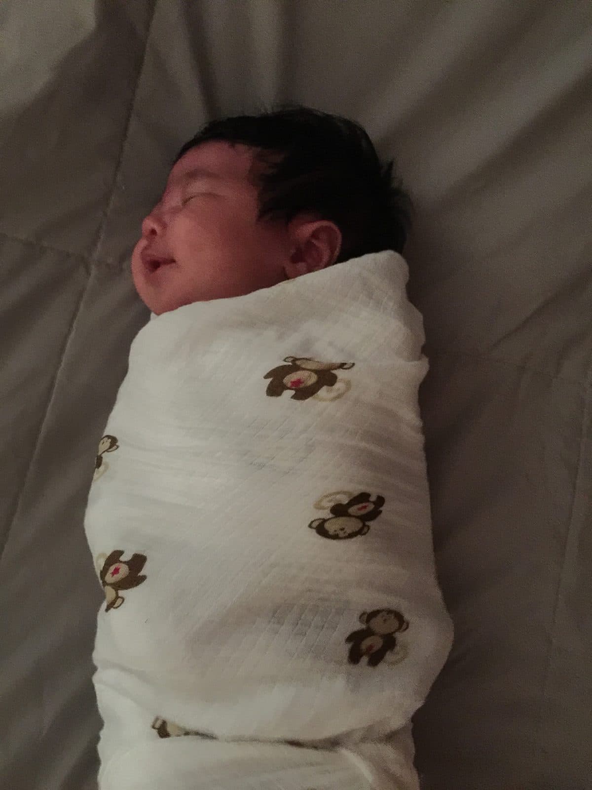 Shan asleep, swaddled snugly with her arms in, in a thin monkey-print muslin