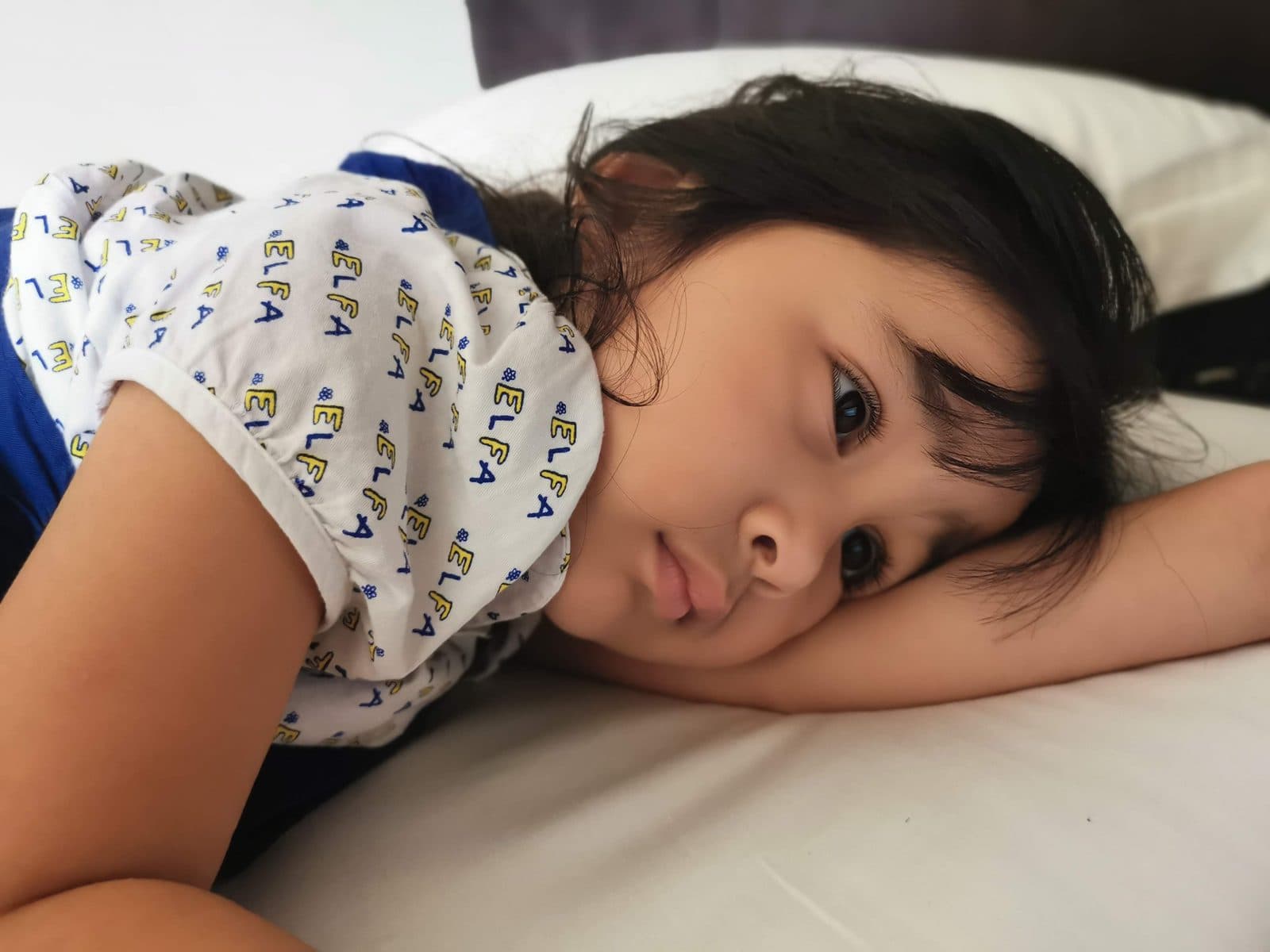 Shan as a young child lying awake on a bed with no blanket over her, head resting on her arm