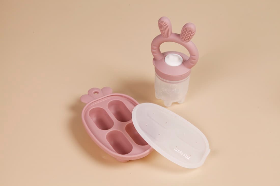 A pink Little Rei fruit feeder and mini freezer tray on a cream background