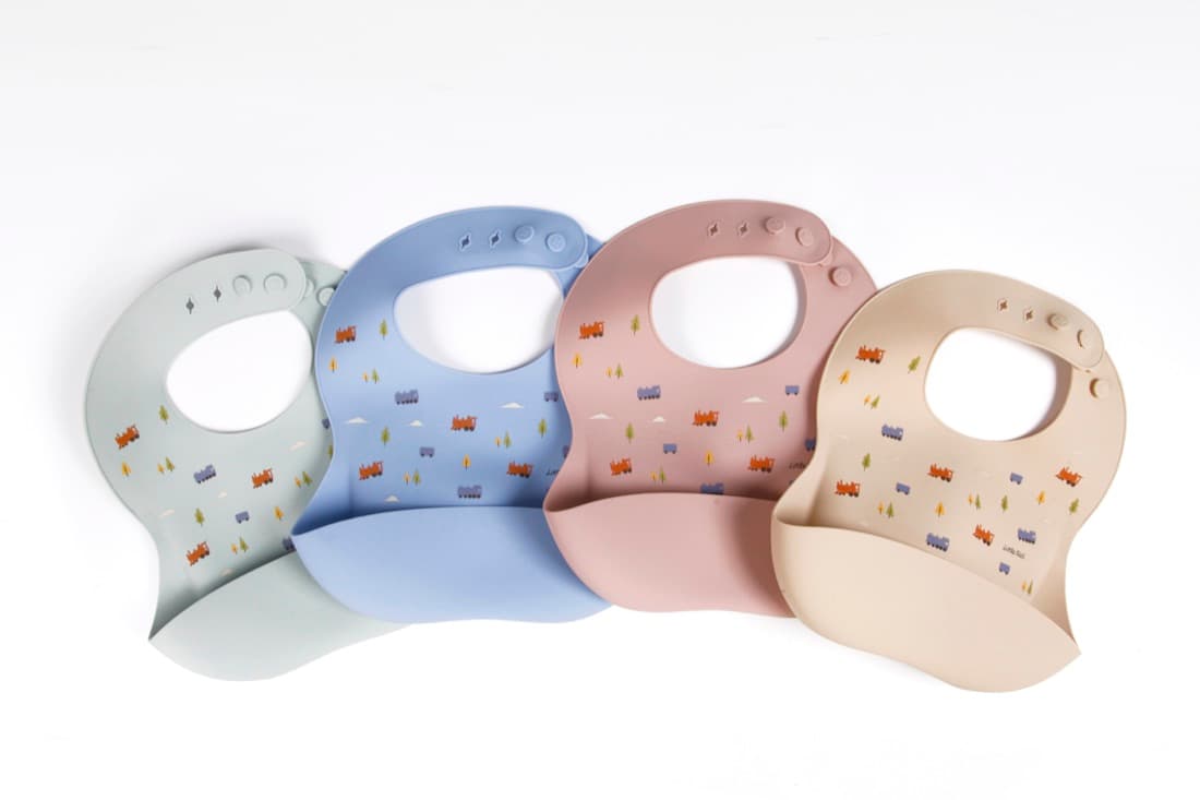 Four Little Rei silicone bibs in sage, blue, rose and sand laid out in a row