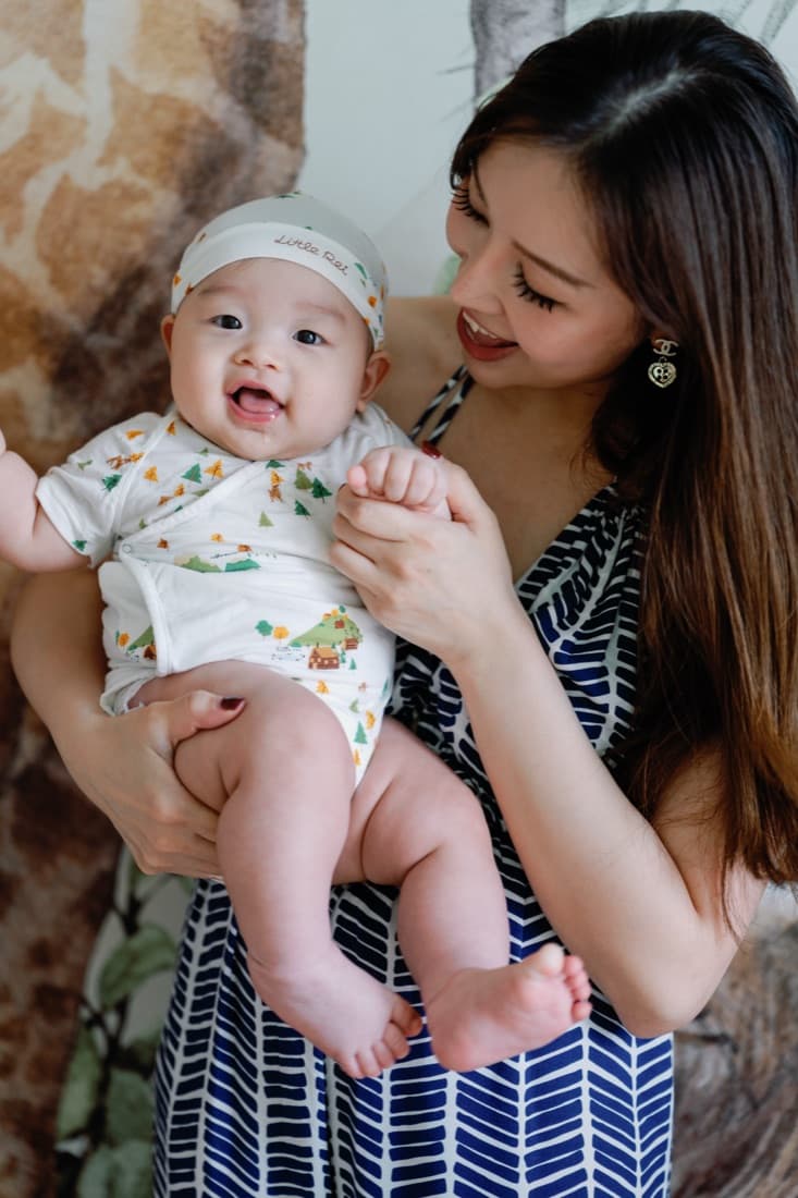 A mother holding her baby up close, the baby smiling and looking towards her face