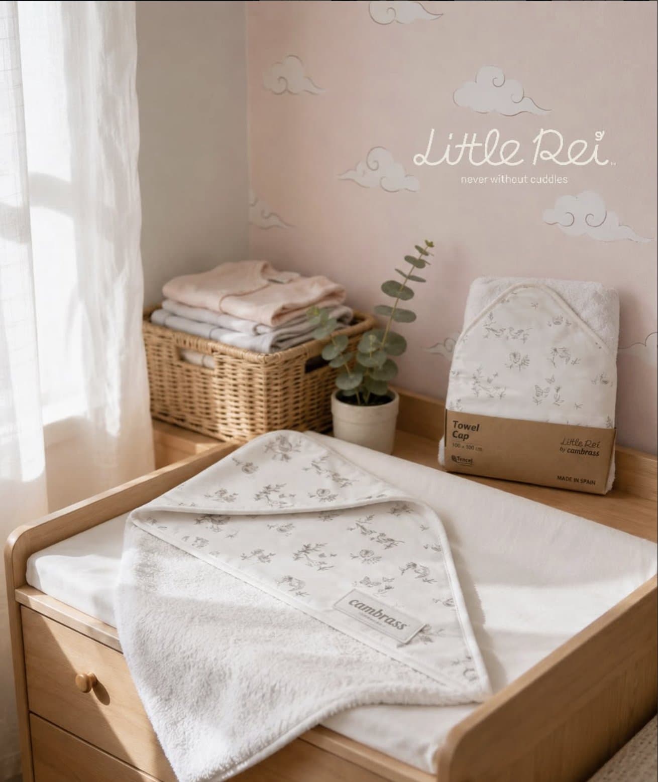 A folded hooded towel on a wooden changing table by a window, with a woven basket and eucalyptus behind
