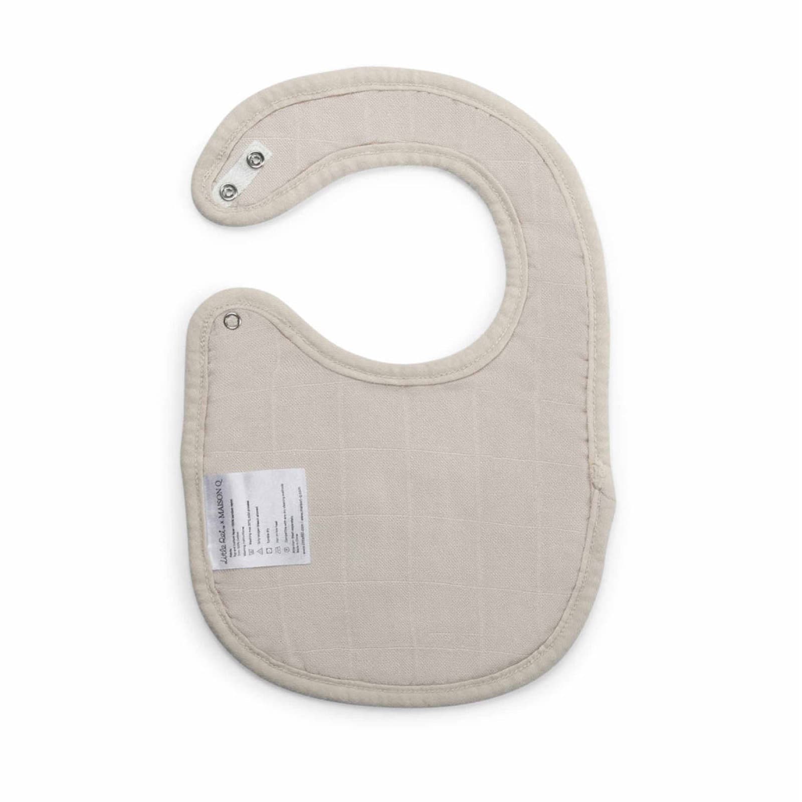 A sand-coloured bamboo muslin bib laid flat, showing its press-stud neck fastening